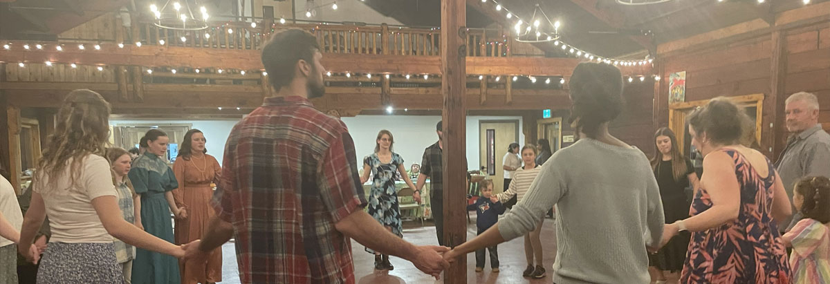 Tab 3: A group of people holding hands in a dance circle with sting lights overhead.