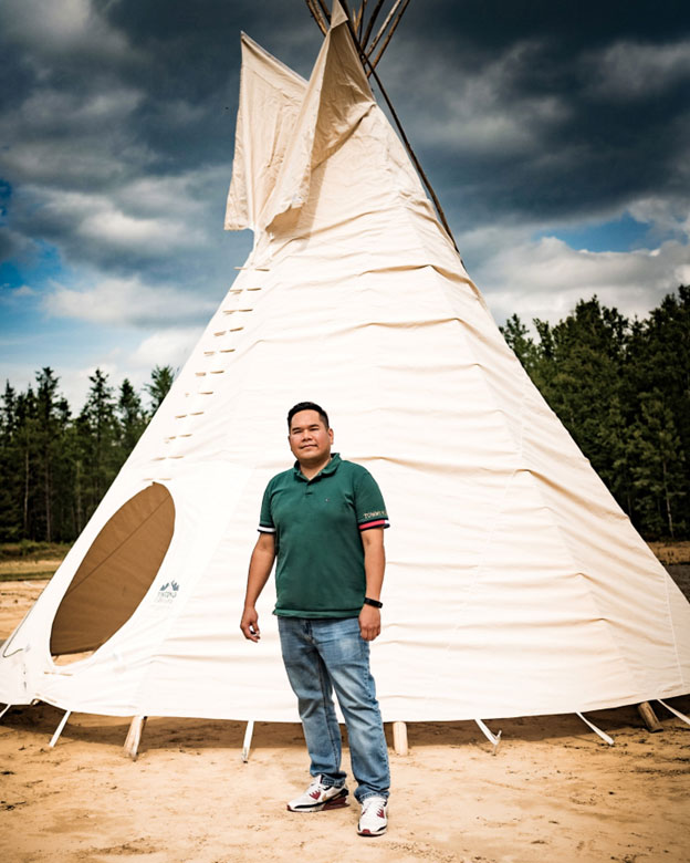 A man stands in front of a tipi.