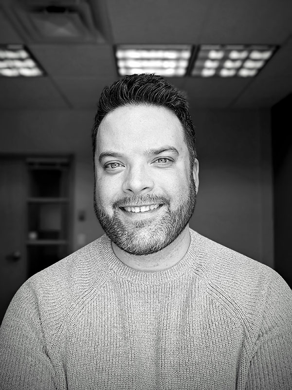 A black and white portrait photograph of a man smiling.
.