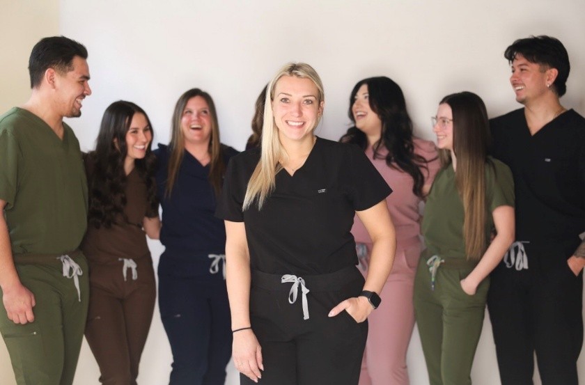 Person wearing black scrubs stands in front of a group of people, all dressed in colorful healthcare uniforms.