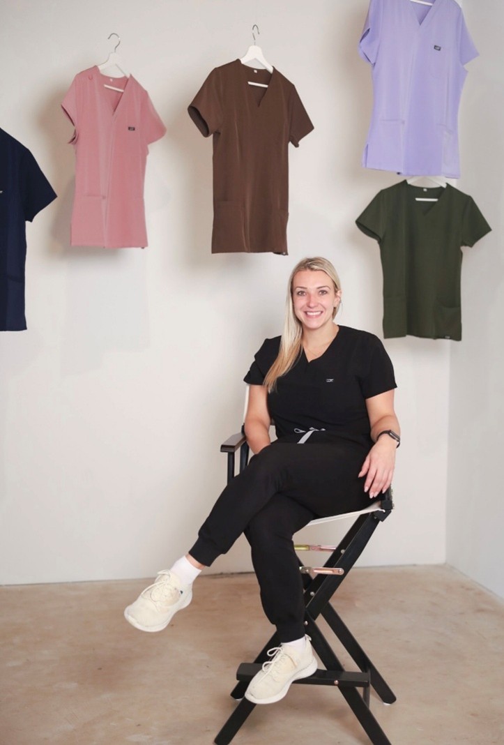 Person wearing black scrubs seated in a director’s chair, confidently representing their healthcare apparel brand in a studio setting.