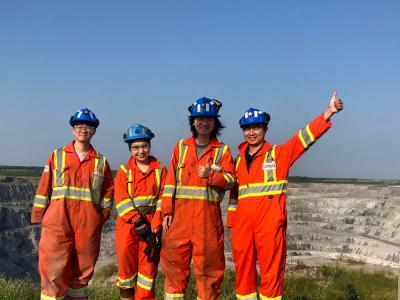 Quatre personnes en vêtements orange sont devant une mine ouverte. Une personne a la main levée.